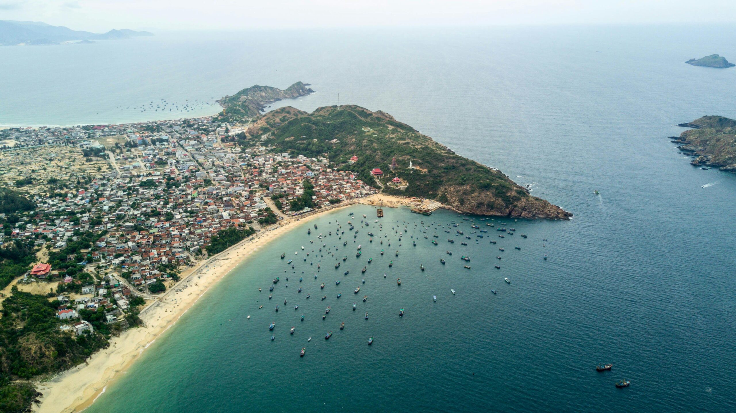 Explore the coastal beauty of Quy Nhon city with its busy harbor and lush green mountains from above.